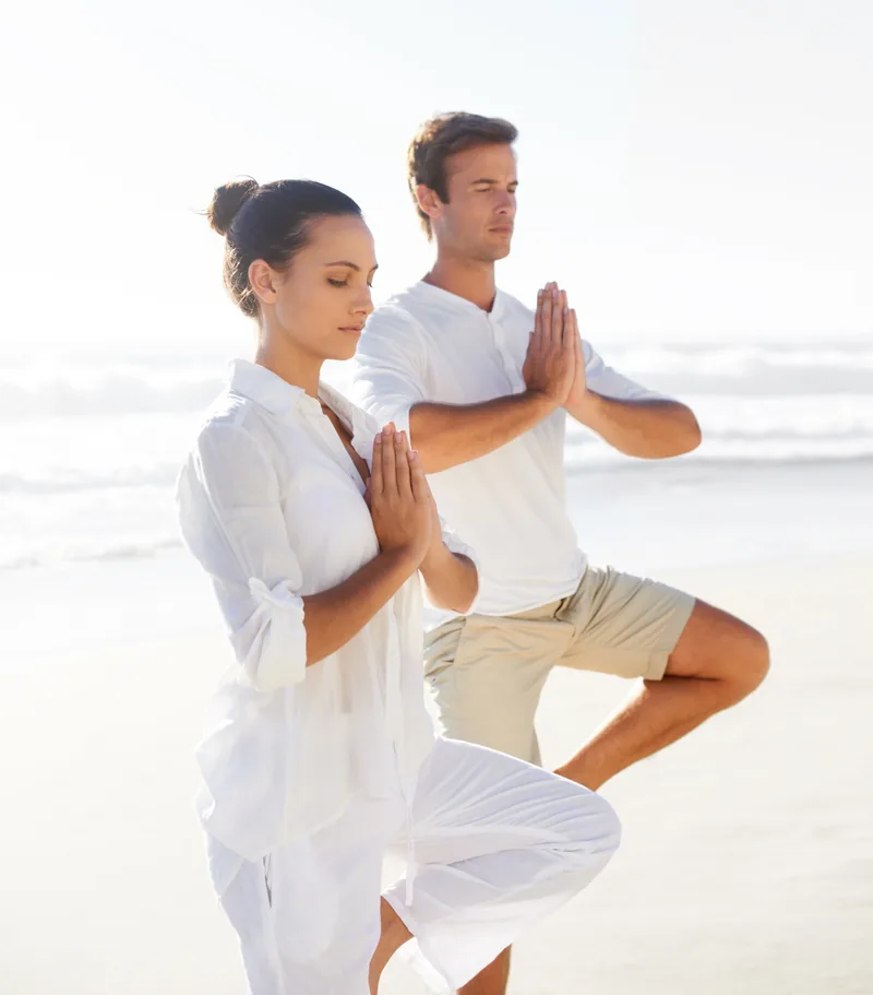 Two People Performing Outdoor Yoga Tree Pose on a Beach for Mindful Wellness
