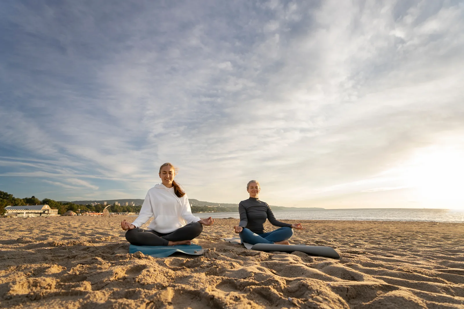 Two People Meditating on the Beach at Sunrise Symbolizing Mental Health Impact